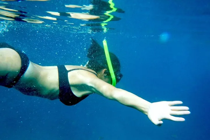 Donna che nuota sott'acqua con attrezzatura da snorkeling in acque blu cristalline.